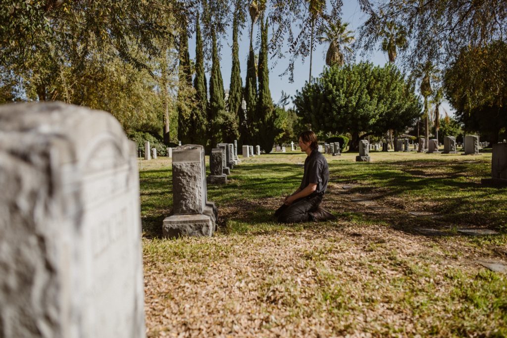 Man kneeling in front of a tombstone representing the death of angus cloud